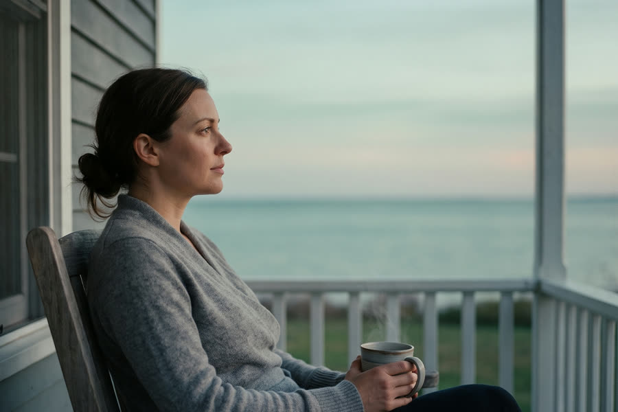 The same woman seated steadily at dawn with tea, looking out at a calm horizon